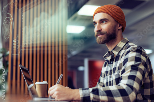 A graphic designer is working with a holographic environment hud surrounding him, projecting his creations over his augmented reality digital user interface. Communicate about future creative business