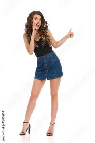 Surprised Sexy Woman In Jeans Mini Skirt And High Heels Is Showing Thumb Up And Talking