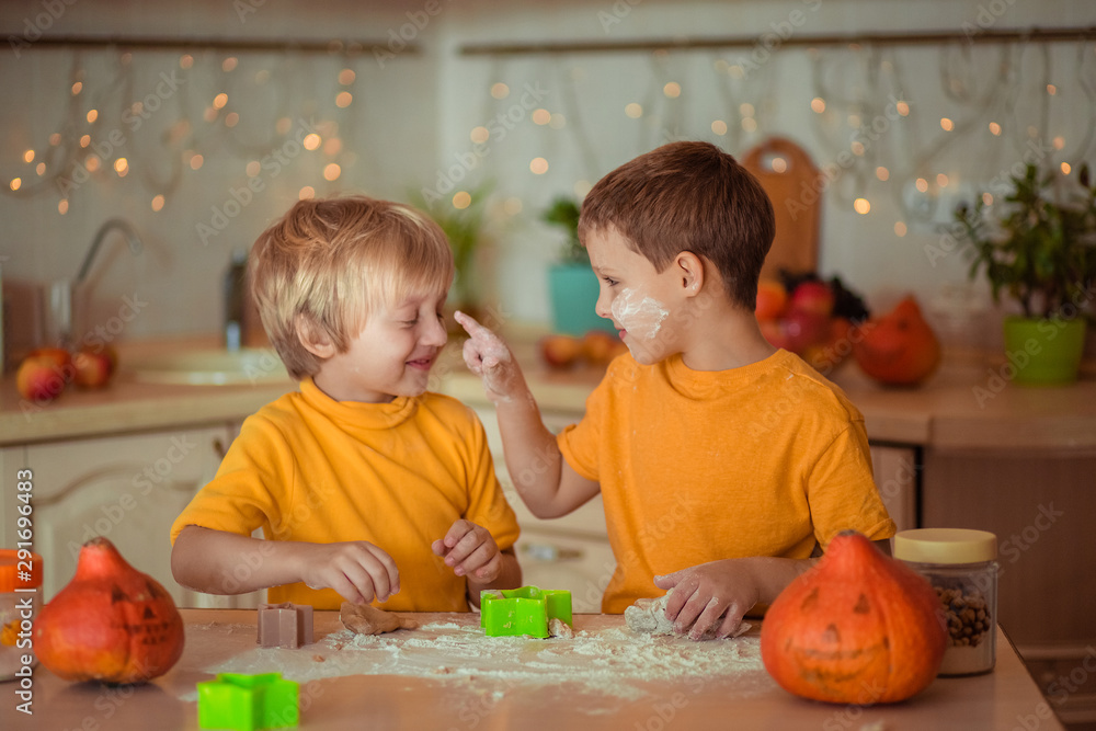 Fototapeta premium Two happy brothers in the kitchen make gingerbread cookies awaiting Halloween.