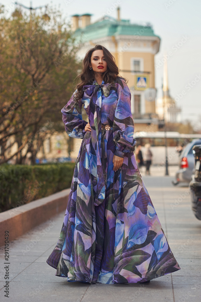 Outdoor fashion style portrait of young tall slim woman in colorful blue chifon dress walking city street. Full length portrait Outdoor fashion style portrait of young tall slim woman in colorful blue chifon dress walking city street. Full length portrait