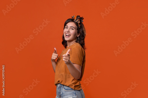 Smiling brunette woman in a t-shirt and beautiful headband pointing with her fingers at the camera isolated over orange background. Place for ad.