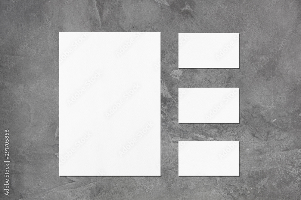 One empty white vertical a4 sized poster and three horizontal rectangle business card mockups with soft shadows on dark grey concrete background. Flat lay, top view One empty white vertical a4 sized poster and three horizontal rectangle business card mockups with soft shadows on dark grey concrete background. Flat lay, top view