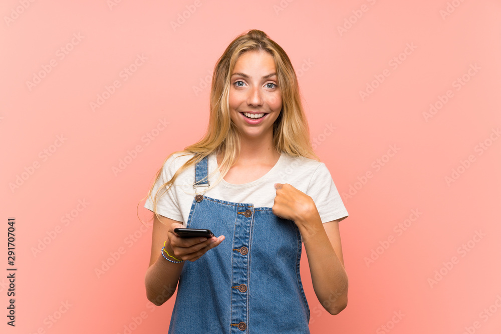 Blonde young woman with a mobile phone over isolated pink wall with surprise facial expression - obrazy, fototapety, plakaty 