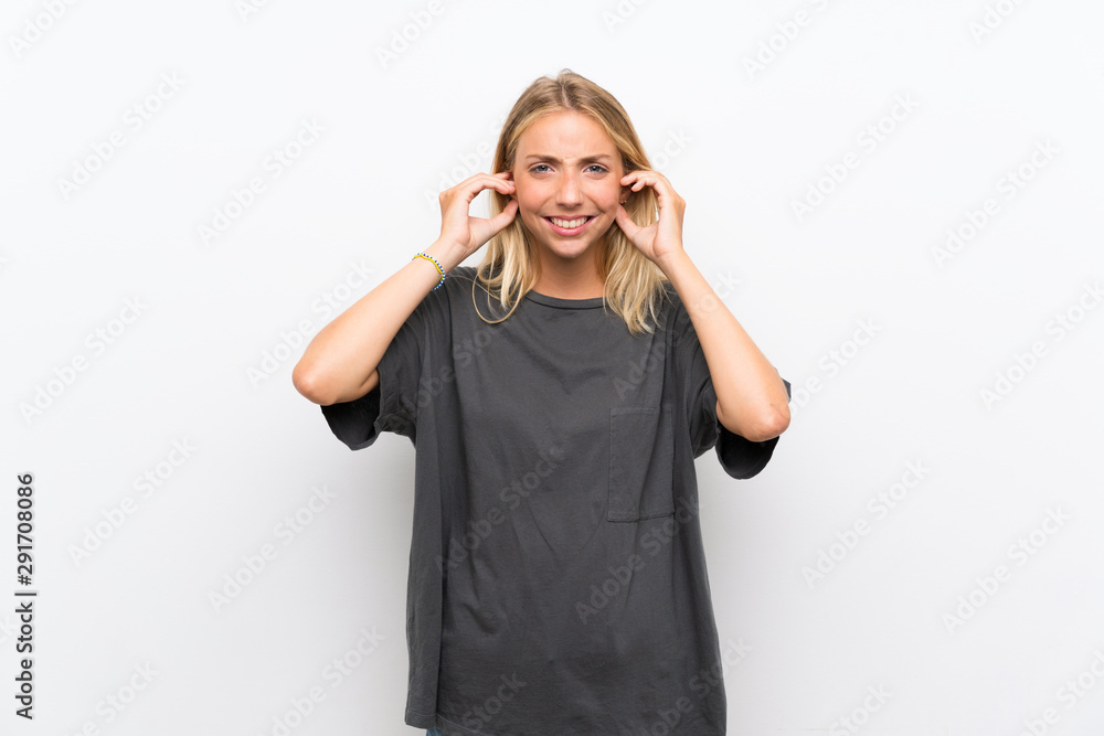 Blonde young woman over isolated white background frustrated and covering ears Blonde young woman over isolated white background frustrated and covering ears