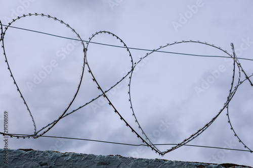 Turns of barb wire on top of aged fence, close up, soft focus. Old concrete wall with barbed wire against dark cloudy sky