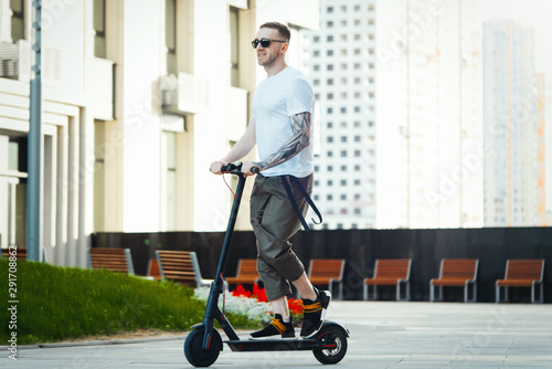 Attractive man riding electric kick scooter at cityscape background.