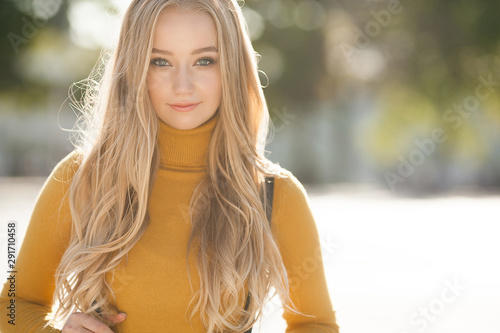 Attractive young blond woman close-up portrait. Female outdoors on autumn sunshine background. Cheerful lady closeup portrait in fall time.