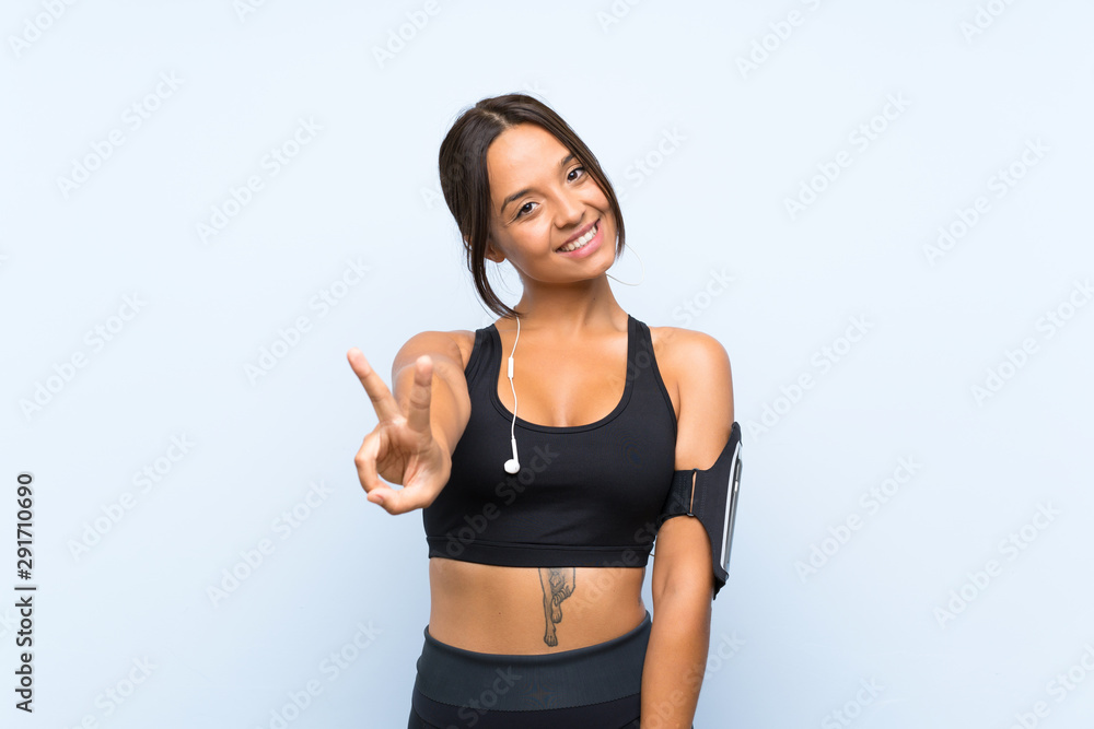Young sport girl over isolated blue background smiling and showing victory sign Young sport girl over isolated blue background smiling and showing victory sign