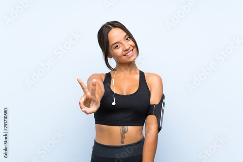 Young sport girl over isolated blue background smiling and showing victory sign © luismolinero