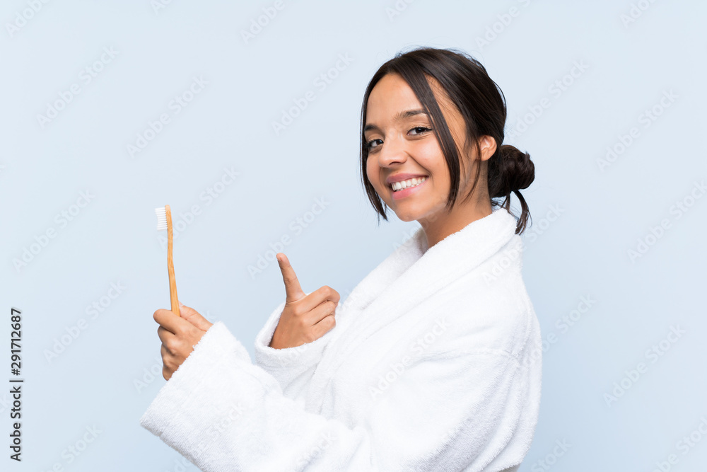 Young brunette woman in bathrobe brushing her teeth over isolated blue background and pointing it Young brunette woman in bathrobe brushing her teeth over isolated blue background and pointing it