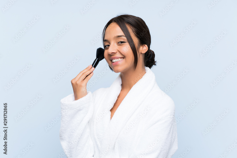 Young brunette girl in bathrobe with makeup over isolated blue background Young brunette girl in bathrobe with makeup over isolated blue background