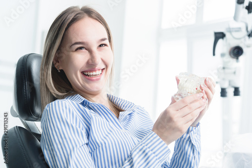 Portrait of a happy attractive girl in a dental chair. Laughing girl at the dentist's appointment with a jaw model in her hands