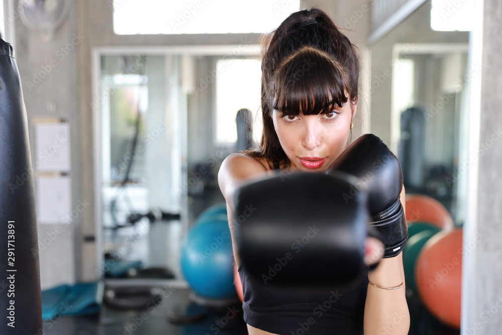 sporty caucasian girl in black sport with black boxer gloves, she punching sandbag