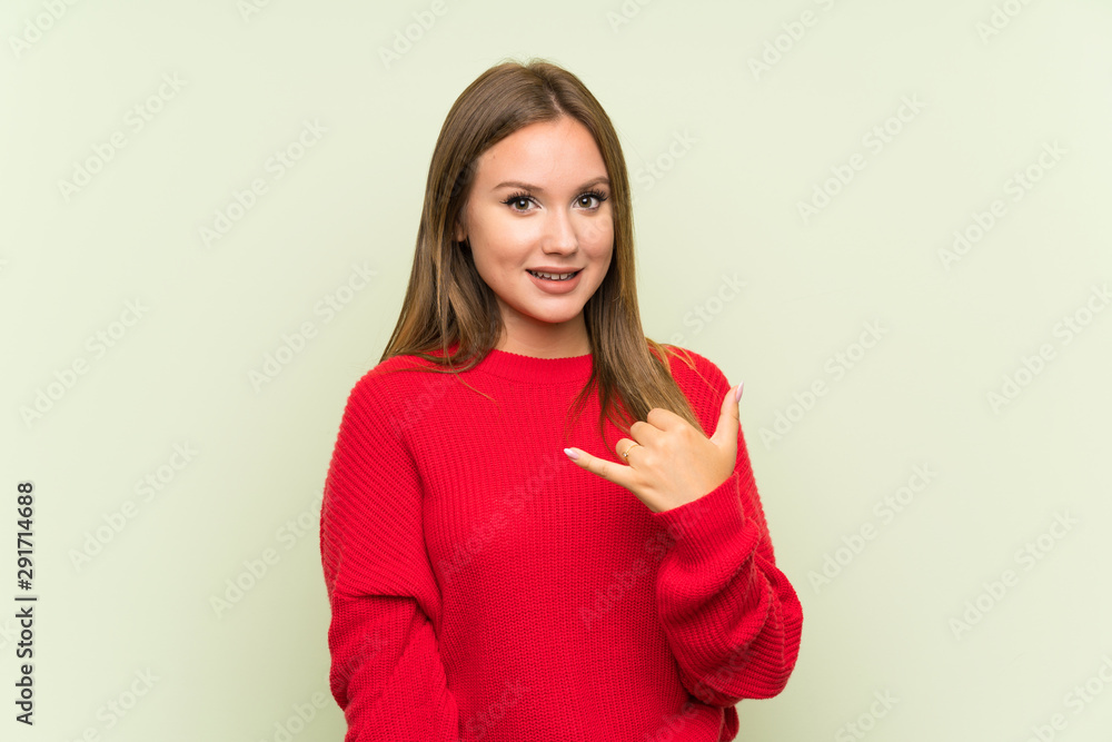 Teenager girl over isolated green background making phone gesture Teenager girl over isolated green background making phone gesture