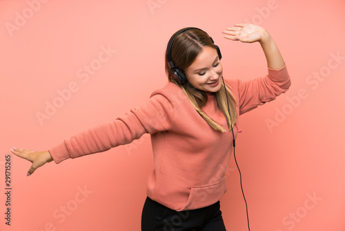 Teenager girl listening music and dancing over isolated pink background