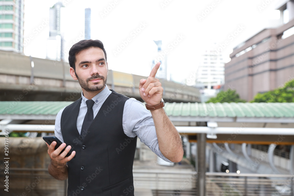 successful caucasian businessman in black suite who standing in downtown, he using cell phone while pointing something with happy smiling face with city and skytrain background successful caucasian businessman in black suite who standing in downtown, he using cell phone while pointing something with happy smiling face with city and skytrain background