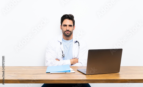 Young doctor man with his laptop over isolated wall keeping arms crossed