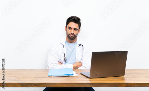 Young doctor man with his laptop over isolated wall thinking an idea