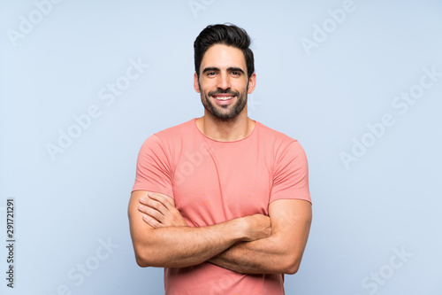 Handsome young man in pink shirt over isolated blue background keeping the arms crossed in frontal position