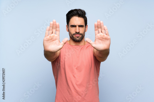 Handsome young man in pink shirt over isolated blue background making stop gesture and disappointed