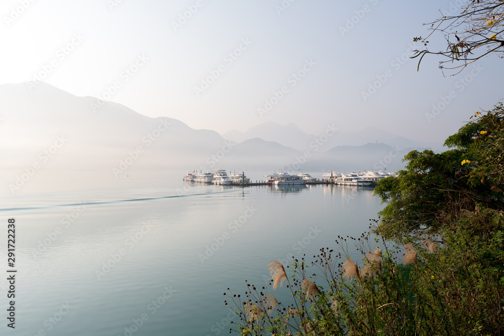 Beautiful tranquil landscape at Sun Moon lake in Nantao, Taiwan. Pier with boats and background of foggy mountains. Concept of peaceful, traanquility of nature.