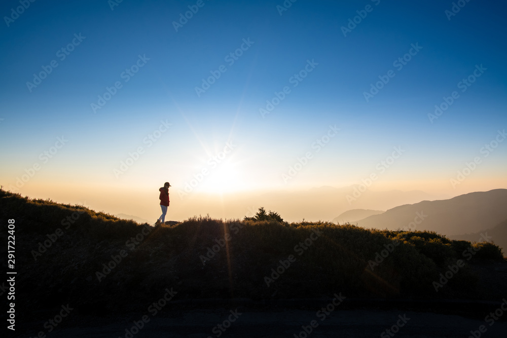 Silhoutte of woman walking on top of the hill with background of sunray during sunset. Concept of hiker, discover, freedom.