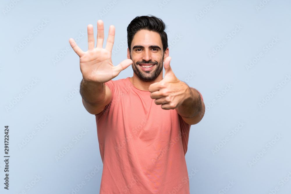 Fototapeta premium Handsome young man in pink shirt over isolated blue background counting six with fingers