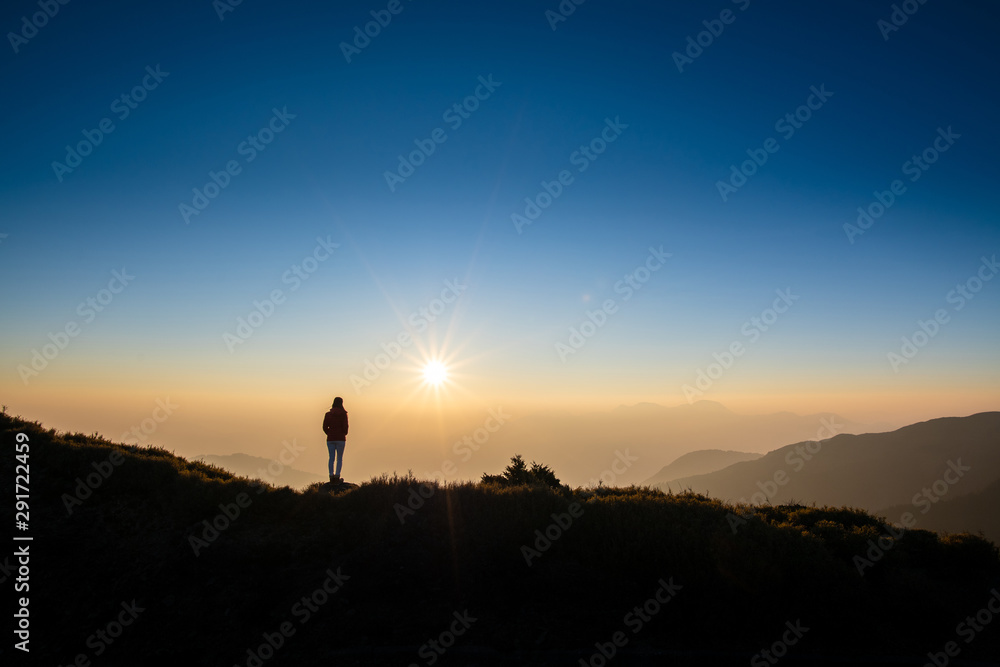 Silhoutte of woman standing on top of the mountain looking at sunset. Concept of successful, discover, wanderlust.