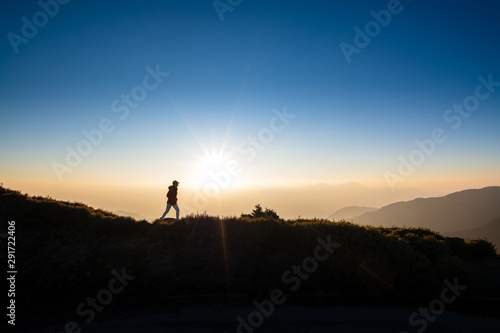 Silhoutte of woman walking on top of the hill with background of sunray during sunset. Concept of hiker, discover, freedom. © 9mot