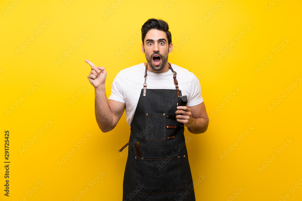 Young hairdresser man over isolated yellow background surprised and pointing finger to the side Young hairdresser man over isolated yellow background surprised and pointing finger to the side