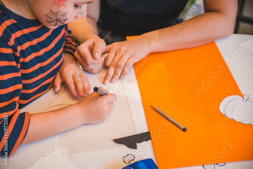 little boy with mother preparing for halloween drawing pumpkin on color paper