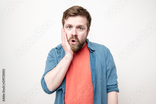 Shocked by the surprise, the bearded man palm hand on his cheek, opened mouth in admiration and made big eyes, on a white background.