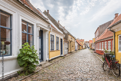 Tableau sur toile A red bike standing alone in an cobblestone street with romantic houses on the i
