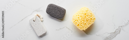 panoramic shot of light and dark gray pumice stone and bath sponge on marble surface