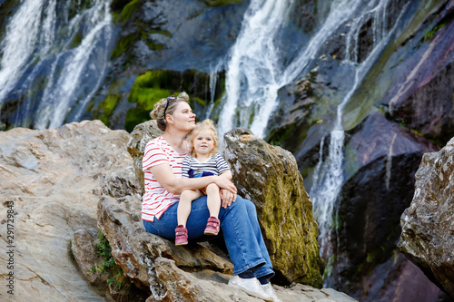 Cute toddler girl and mother sitting near water cascade of Powerscourt Waterfall, the highest waterfall in Ireland in co. Wicklow. Family time vacations with small children. Woman and baby child photo