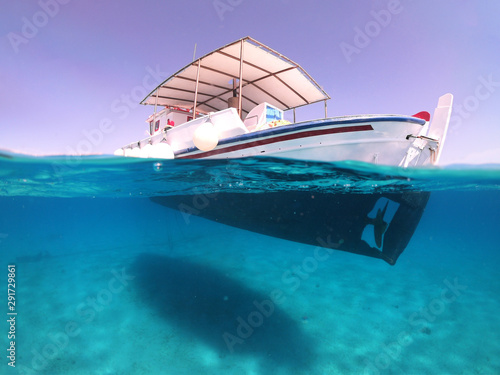 Above and below underwater photo of traditional fishing boat docked in turquoise clear sea, Mykonos island, Cyclades, Greece