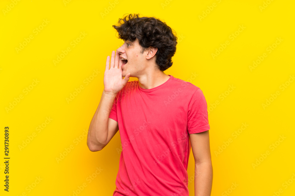 Young man over isolated yellow wall shouting with mouth wide open Young man over isolated yellow wall shouting with mouth wide open