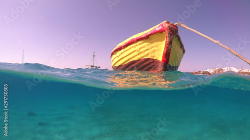 Above and below underwater photo of traditional fishing boat docked in turquoise clear sea in port of Koufonisi island, Small Cyclades, Greece