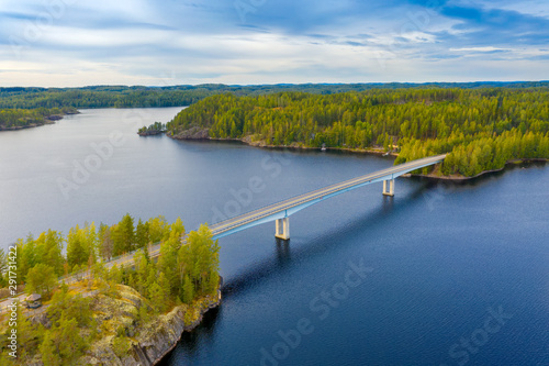 Aerial view of the bridge and island on a blue lake Saimaa. Landscape with drone. Blue lakes, islands and green forests from above on a cloudy summer morning. Lake landscape in Finland.