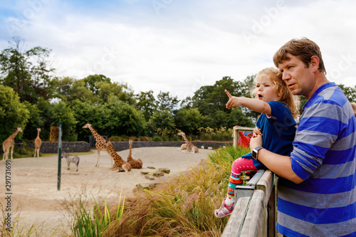 Photography Cute adorable toddler girl and father watching and feeding giraffe in zoo