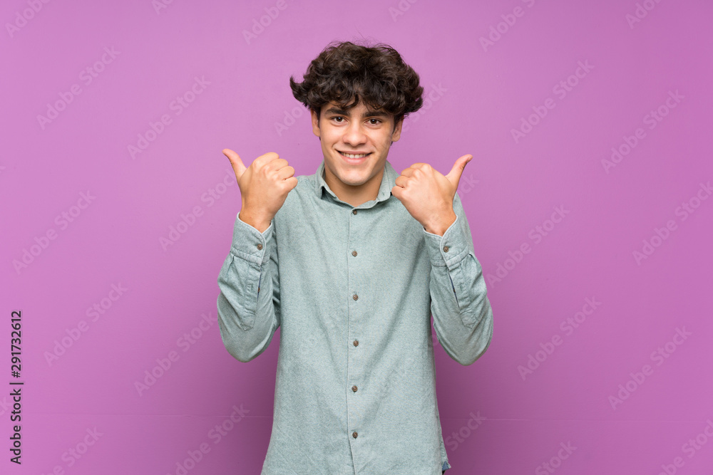Young man over isolated purple wall with thumbs up gesture and smiling Young man over isolated purple wall with thumbs up gesture and smiling