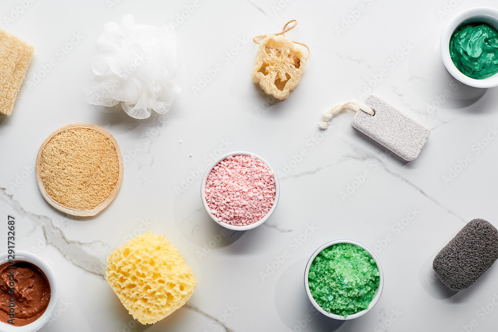 top view of color bath sponges, pumice stones, bath salts and clay mask on marble surface