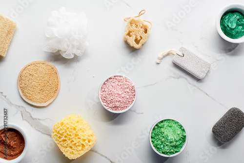 top view of color bath sponges, pumice stones, bath salts and clay mask on marble surface
