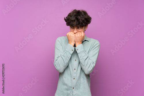 Young man over isolated purple wall nervous and scared putting hands to mouth © luismolinero