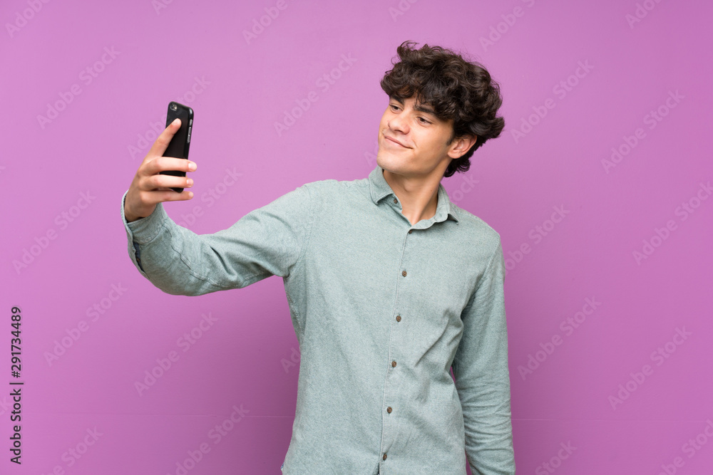 Young man over isolated purple wall making a selfie Young man over isolated purple wall making a selfie