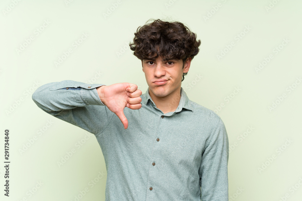 Young man over isolated green wall showing thumb down sign Young man over isolated green wall showing thumb down sign