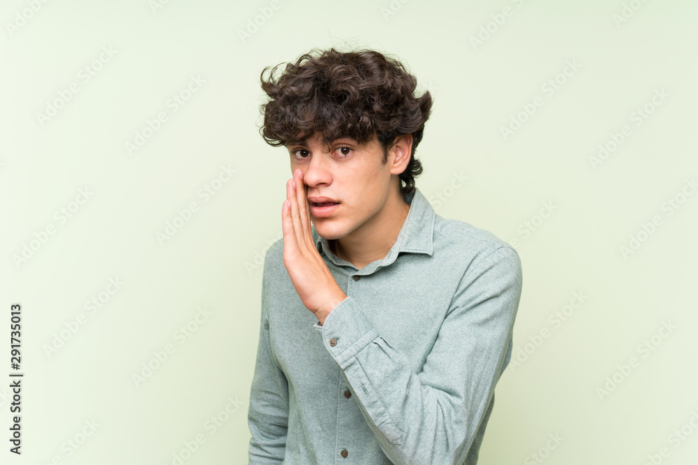 Young man over isolated green wall whispering something Young man over isolated green wall whispering something