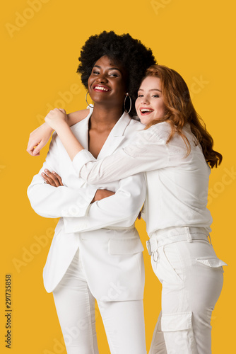 smiling redhead girl hugging african american woman isolated on orange