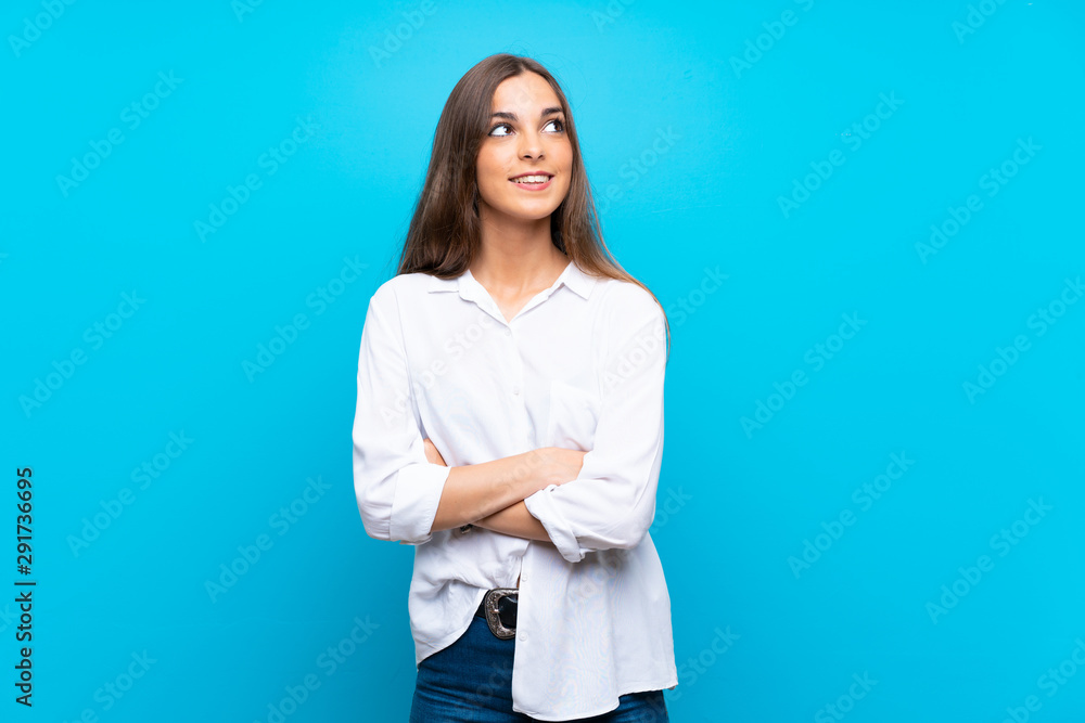 Young woman over isolated blue background looking up while smiling Young woman over isolated blue background looking up while smiling