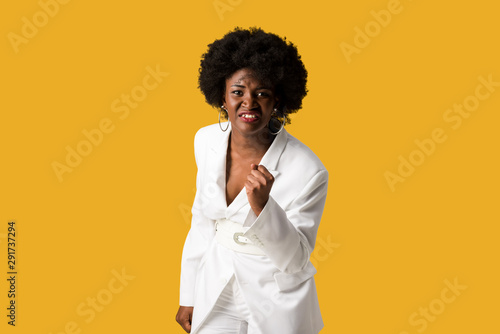 frustrated and curly african american girl standing with clenched fist isolated on orange